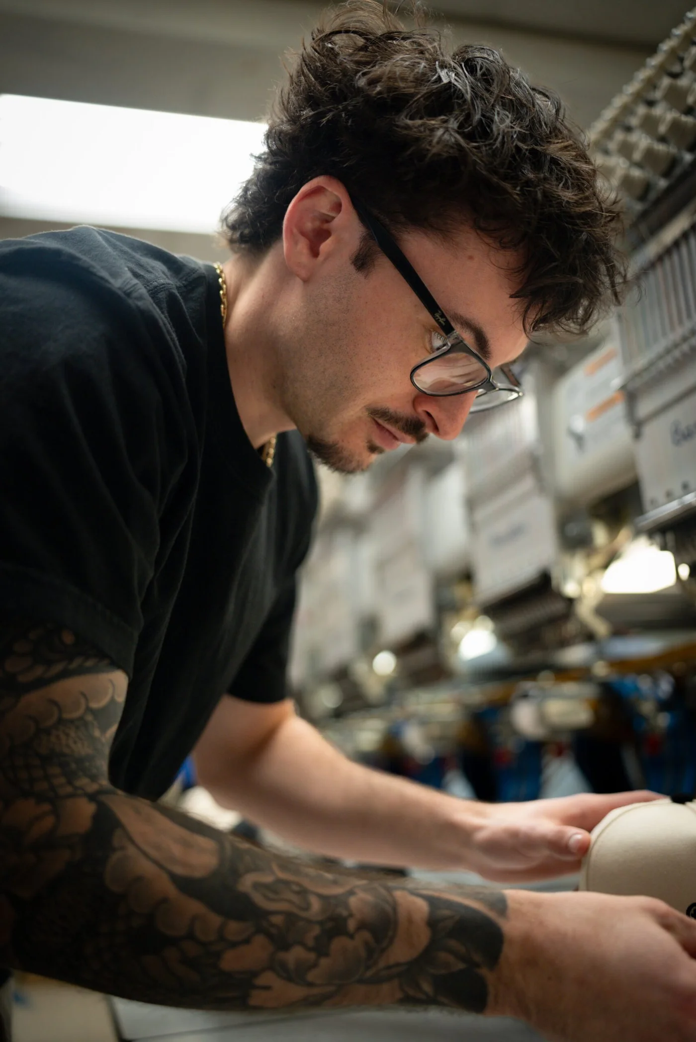 A team member working on a cap beside embroidery equipment